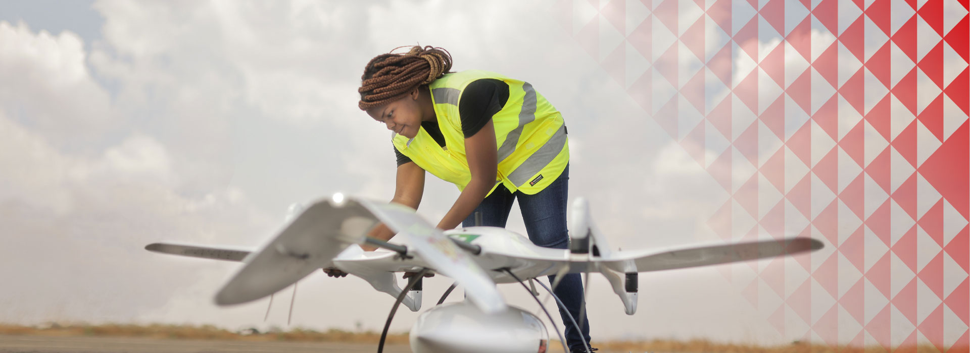 A woman in a high visibility vest is working on a drone.