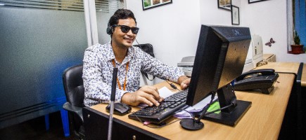A blind man is working at a computer in an office.