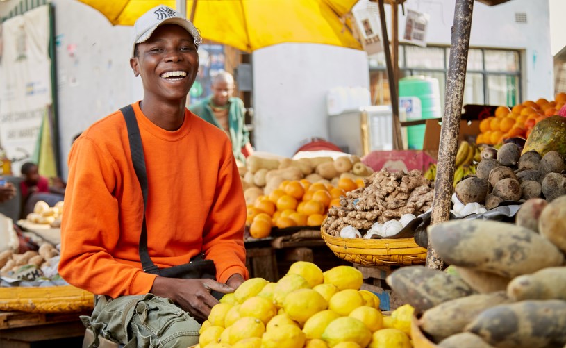 A person smiling at a fruit stand.