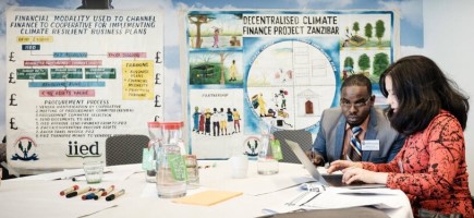 Two people work on a laptop. Posters on climate issues are displayed in the background.