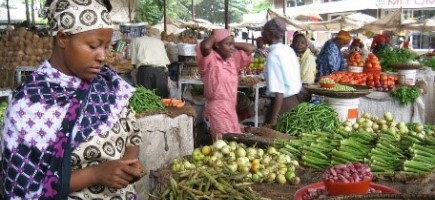 A woman looks at vegetables on a market stall.