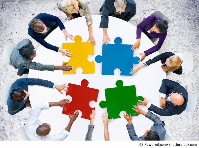 Bird's eye view of several persons sitting around a white table with four large puzzle pieces in primary colours