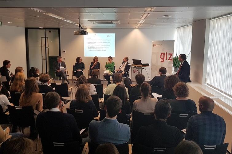 5 Personen sitzen auf Stühlen auf einer Bühne mit Publikum