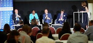 Vier Personen sitzen auf Stühlen nebeneinander auf einer Bühne