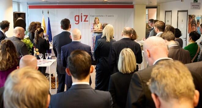 Viele Personen stehen in einem Raum und hören vorne einer Person zu