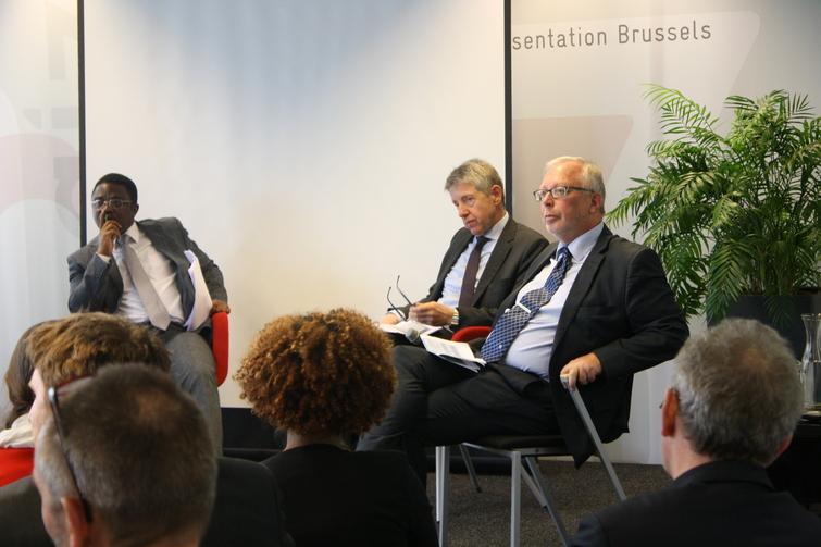 Drei Männer sitzen auf Stühlen vor einem Publikum