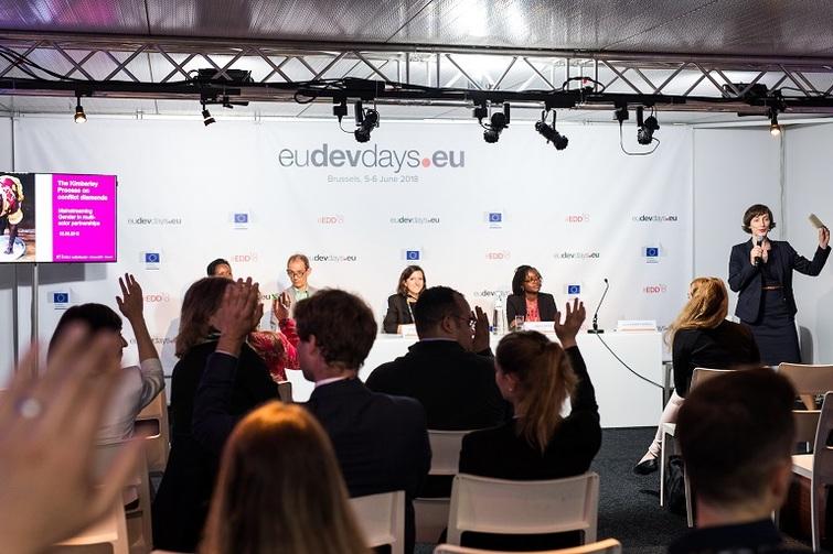 Personen sitzen vorne gemeinsam an einen Tisch. Publikum sitzt ihnen gegenüber