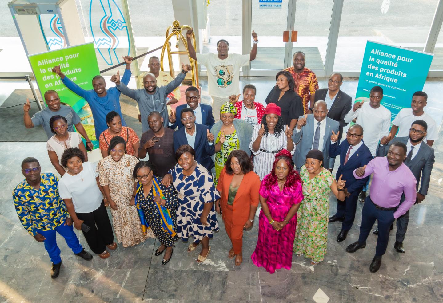 A large group of people pose together indoors at a “Quality Boost” event, smiling and raising their hands in celebration.