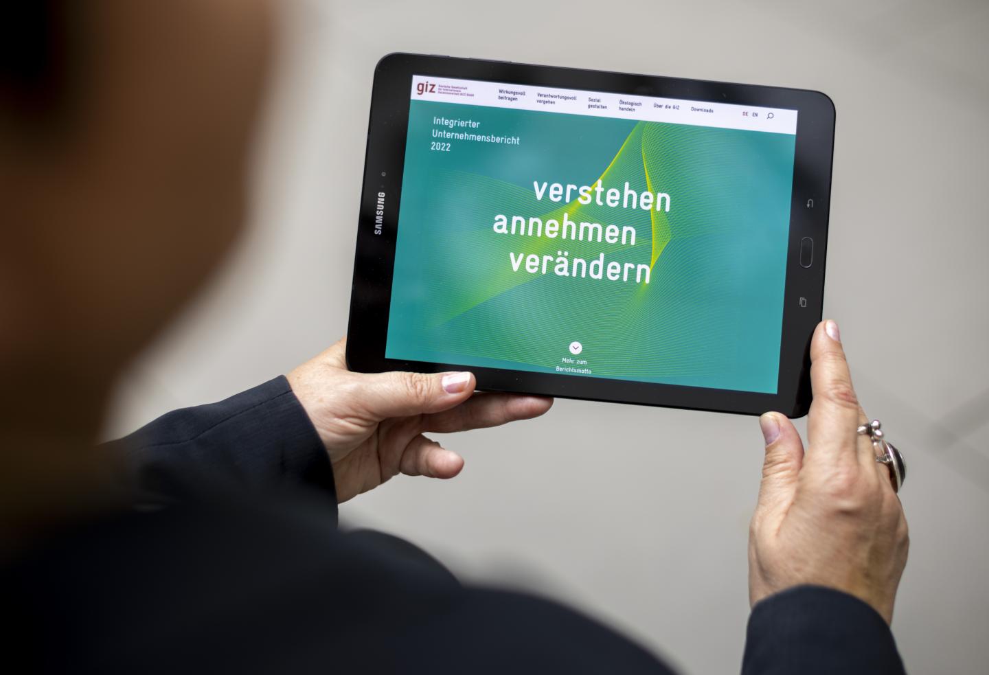 Zwei Hände halten einen Tablet-Computer, der die erste Seite des Integrierten Unternehmensberichts 2022 der GIZ zeigt.