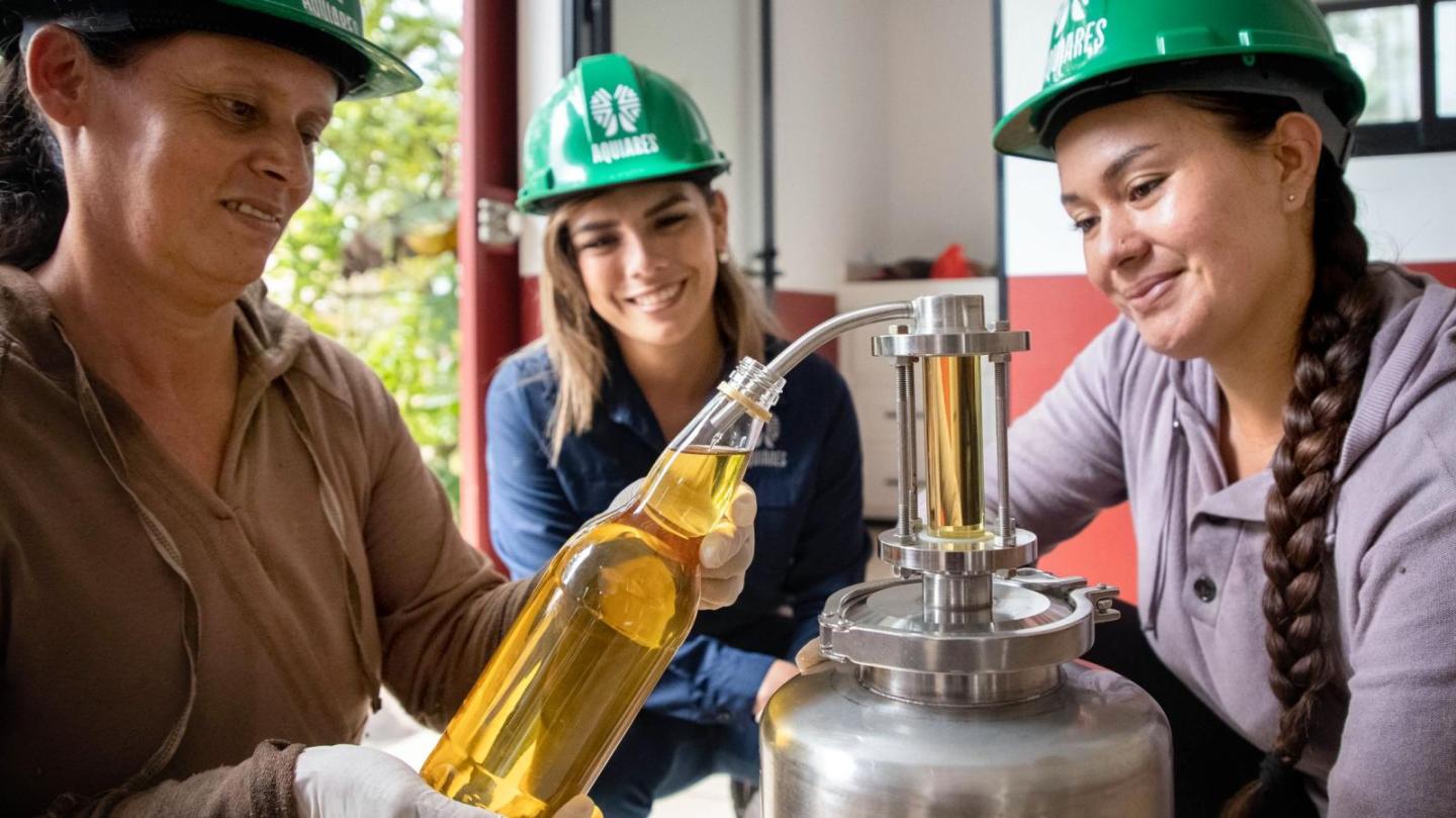 A woman fills a bottle with oil while two other women watch.