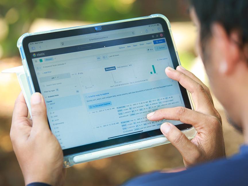 Eine Person hält ein Tablet und analysiert Daten auf einem Dashboard der Plattform Elastic, mit sichtbaren Grafiken und Texten zur Dokumentensuche.