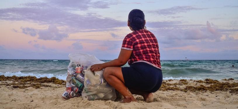 Eine Frau sitzt an einem Strand in Mexiko, neben zwei vollen Müllsacken, die sie zuvor gesammelt hat.