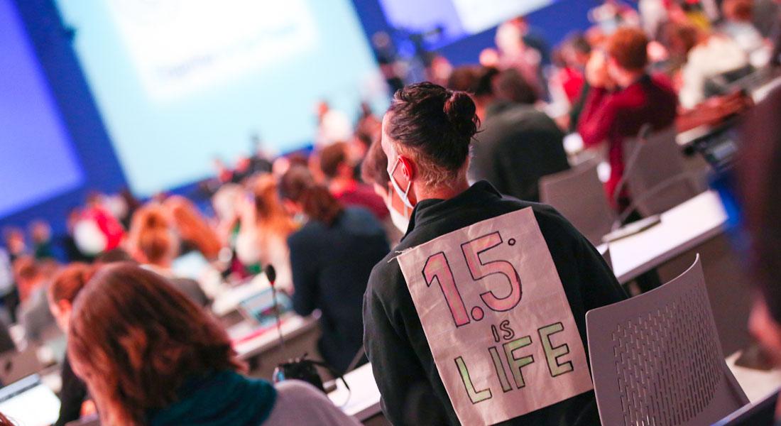 Conference with a view of people's backs. Person in the foreground is carrying a sign with the words ‘1.5° is Life’ on their back.