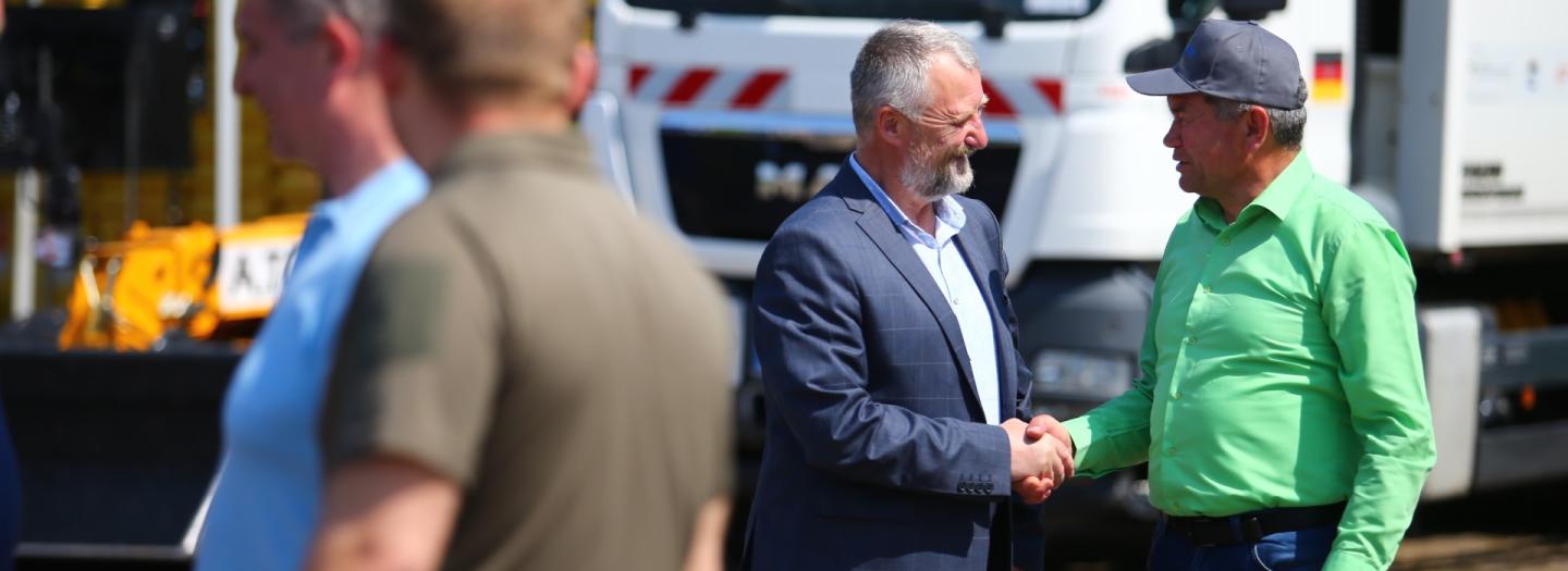 Zwei Männer stehen vor einem Müllauto und schütteln sich die Hand.