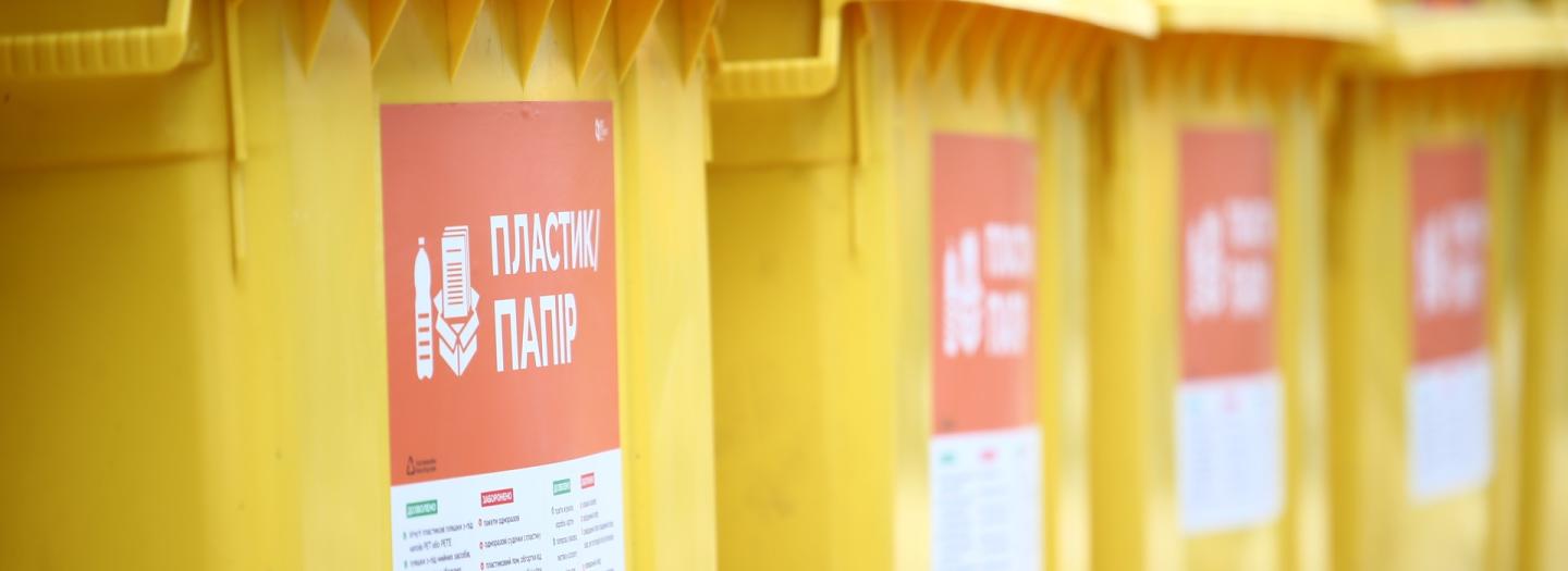 Eine Reihe gelber Mülltonnen mit Beschilderungen darauf.