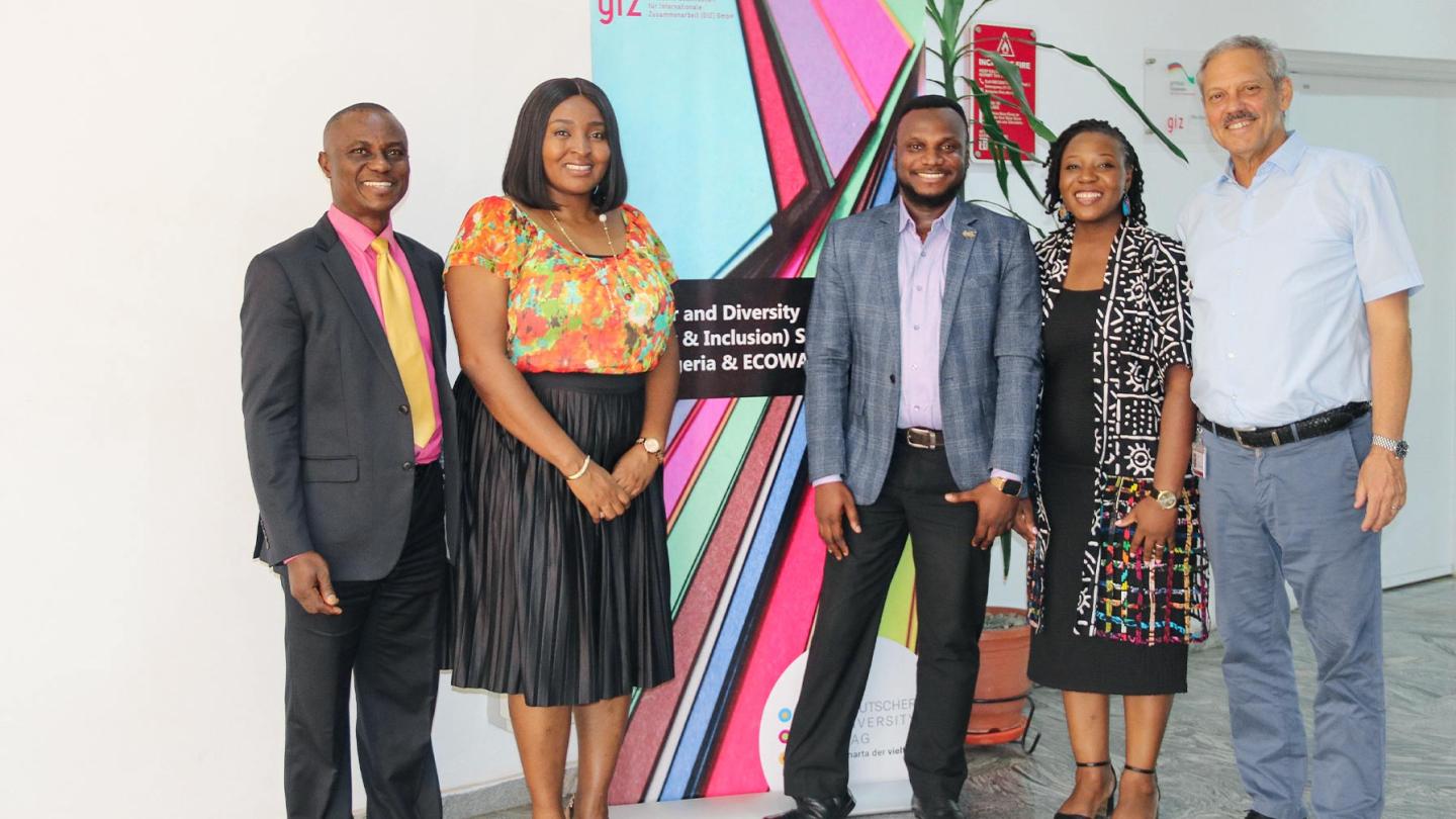 Five people standing in front of a roll-up banner on ‘Gender and Diversity Strategy – Nigeria & ECOWAS’; they are smiling at the camera.