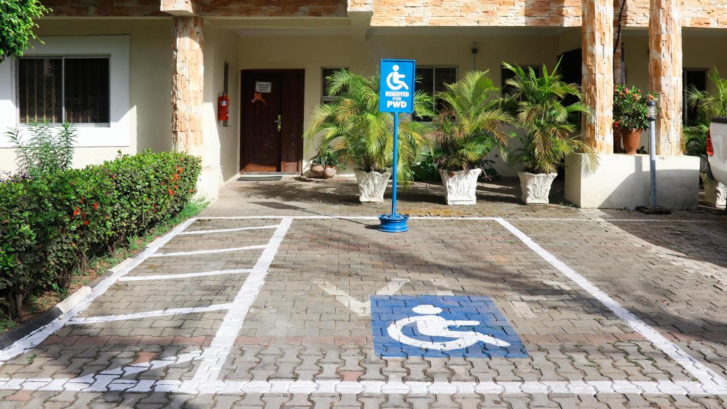 A designated parking space for people with disabilities in front of a building, indicated by markings on the ground and an information sign.