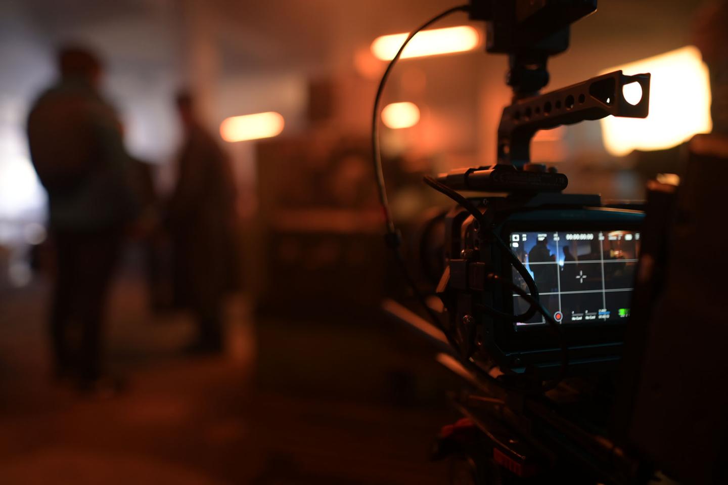 A camera is pointed at several people and films the scene. 