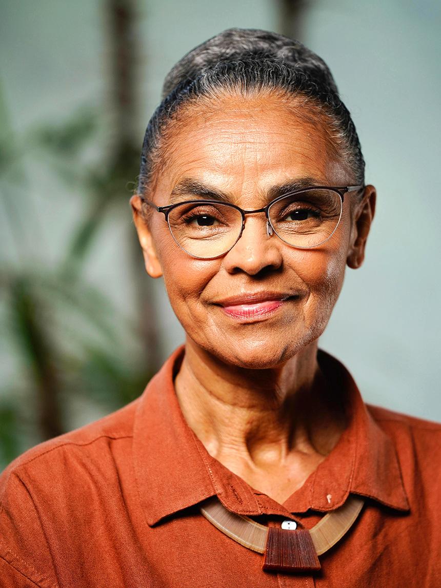 Portrait of a smiling woman with glasses and a brown blouse wearing a distinctive necklace.