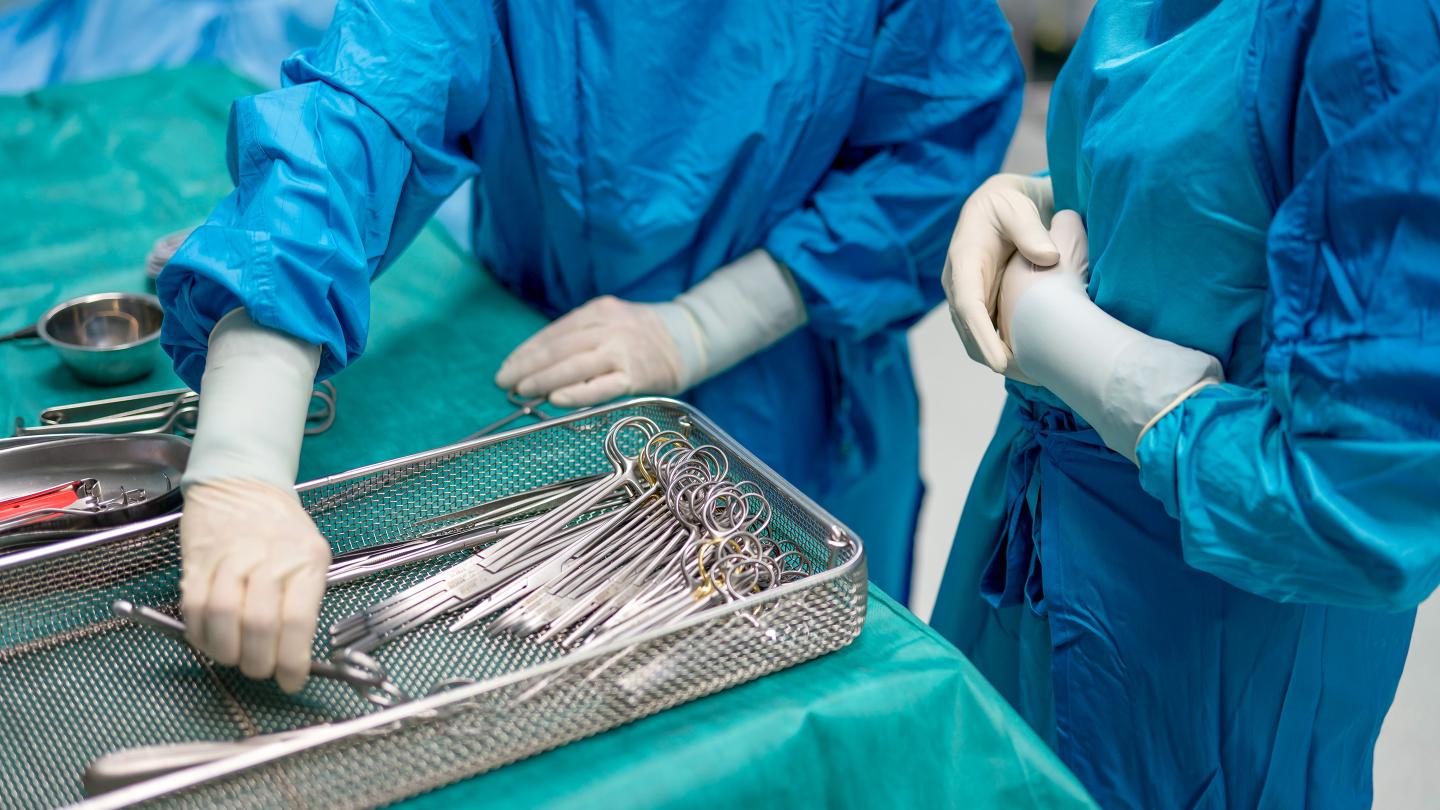 Two people in blue surgical gowns arrange surgical instruments on a sterile table.