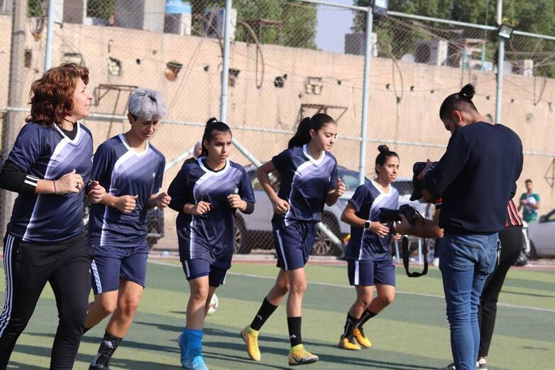 Women and men stand left and right and smile at the camera. A woman walks between them. Copyright: GIZ