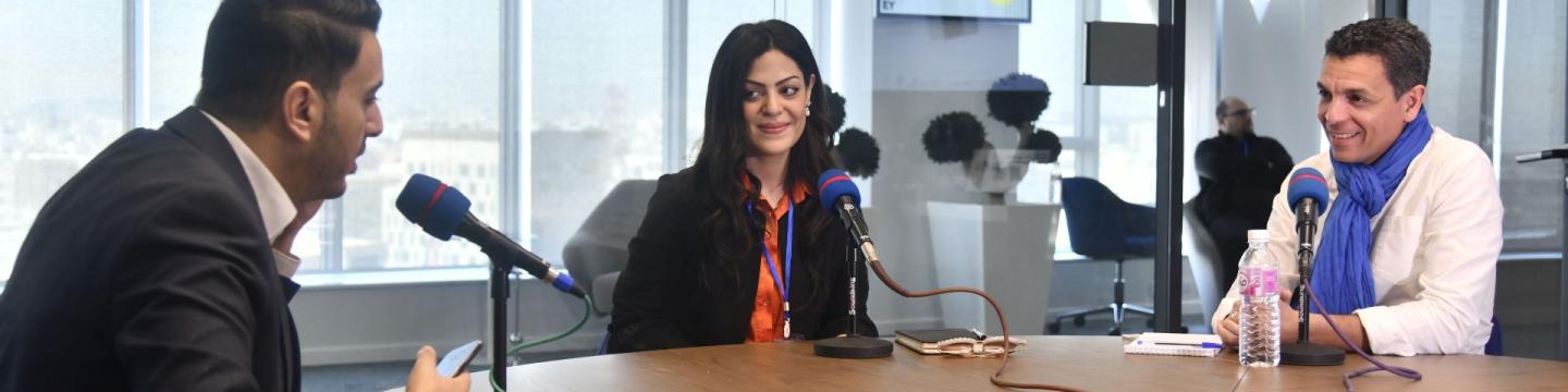 Eine Person, die an einem Tisch mit Mikrofonen sitzt.