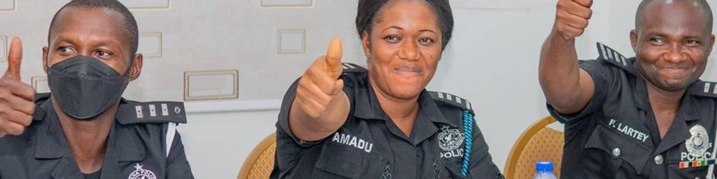 Polizist*innen aus Ghana sitzen bei einem Workshop zusammen und halten Daumen hoch.