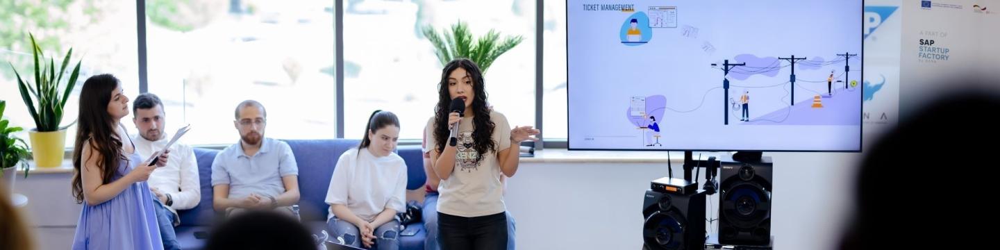 Eine Frau spricht während einer Präsentation eines Start-up-Pitchs in ein Mikrofon.