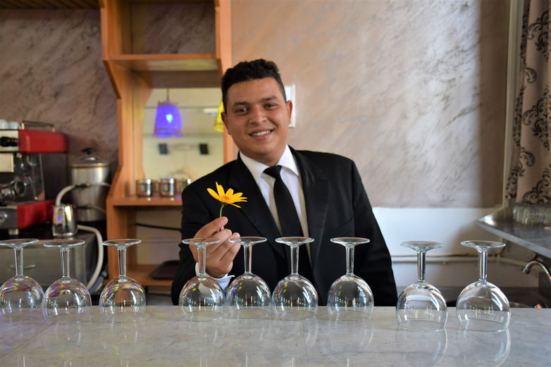 Ein junger Mann steht hinter einer Restauranttheke und hält eine Blume.