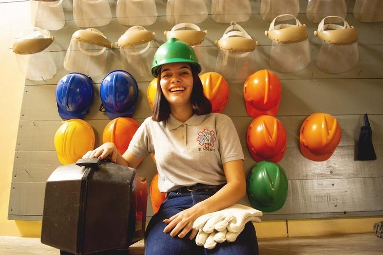 Joven frente a una pared con cascos protectores. © GIZ-INBAS