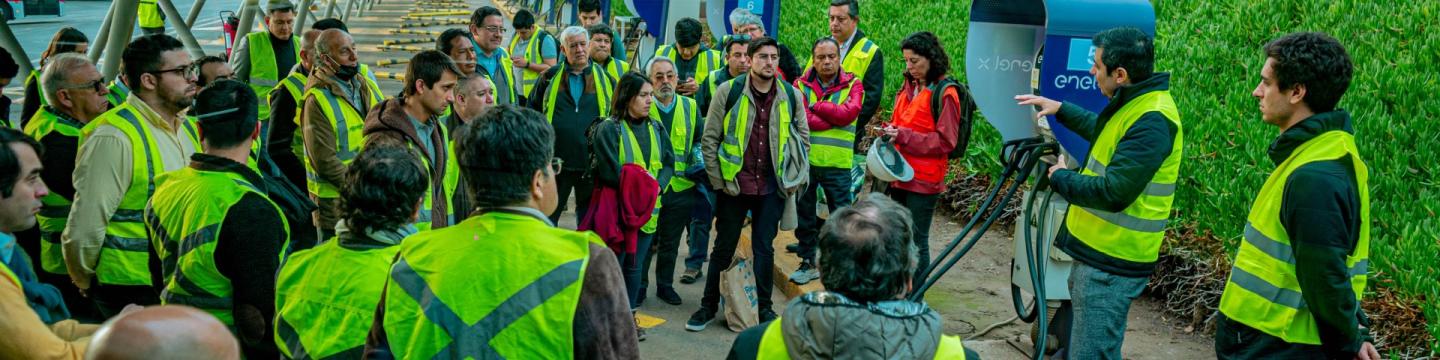 Ein Mann erklärt einer Gruppe eine E-Ladesäule an einem Elektrobusbahnhof.