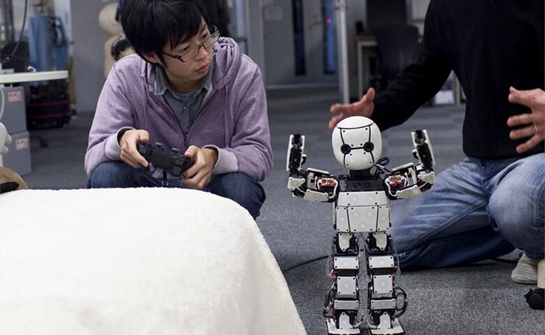 A young student using a game controller to program a humanoid robot in a technical course setting.