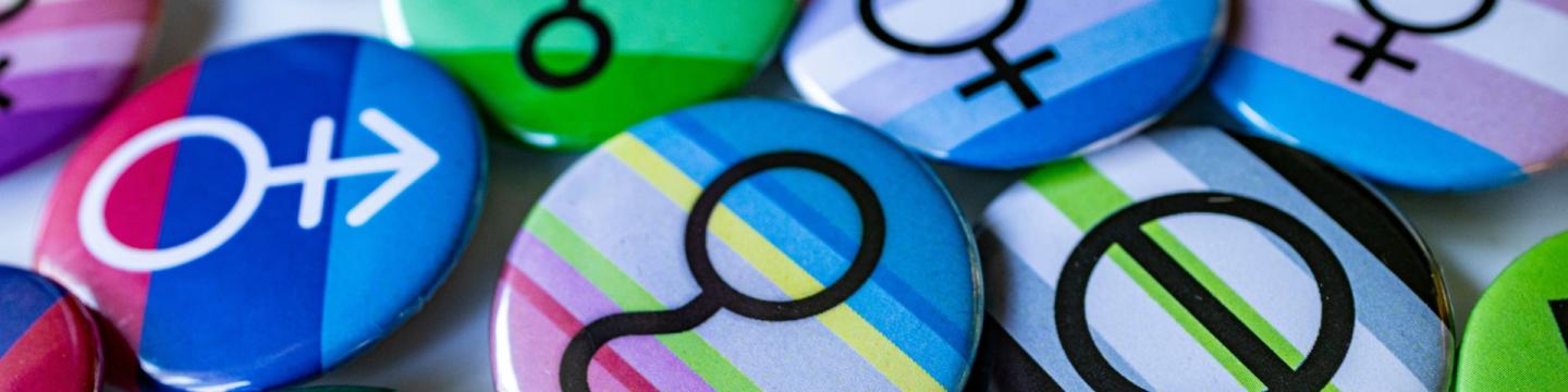 Bunte Abzeichen mit Geschlechtersymbolen auf Stolzflaggen, die für Vielfalt, Gleichberechtigung und Integration stehen.