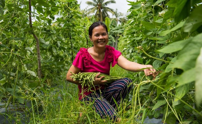 A woman harvests in her field, smiling at the camera.