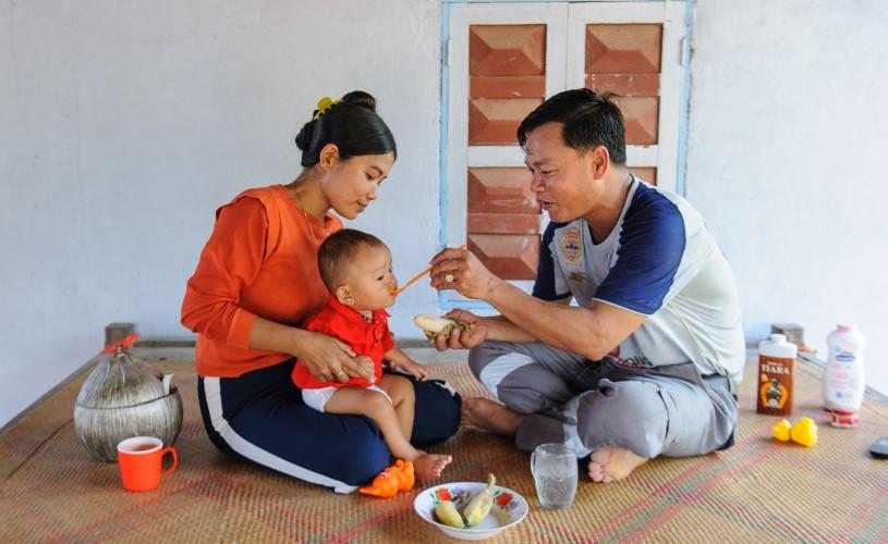 A mother has her child on her lap being fed by its father.