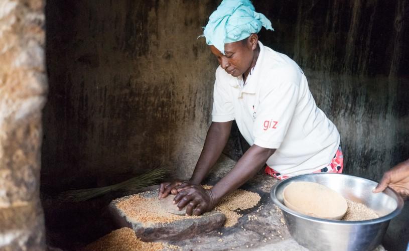 A woman crushes grains with the help of a stone.