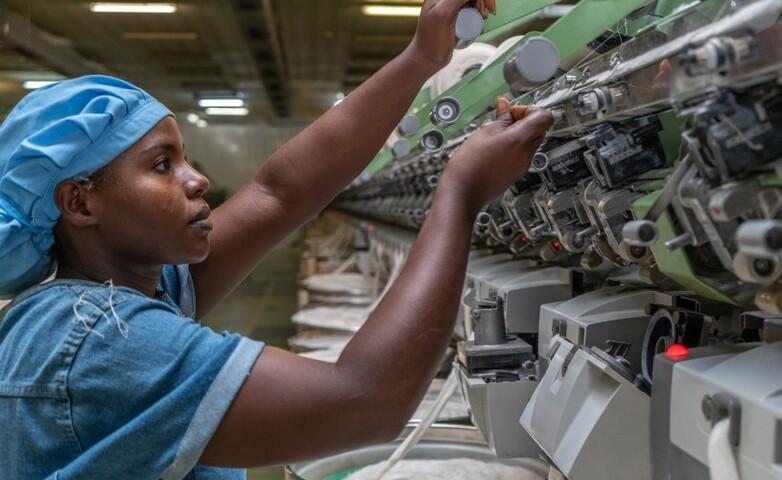 Eine Arbeiterin, die eine Spinnmaschine in einer Textilfabrik bedient und die Fäden an der Maschine justiert.