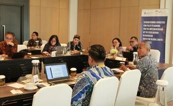 Teilnehmende diskutieren an einem Tisch, im Hintergrund sind Laptops und ein Banner zu sehen.