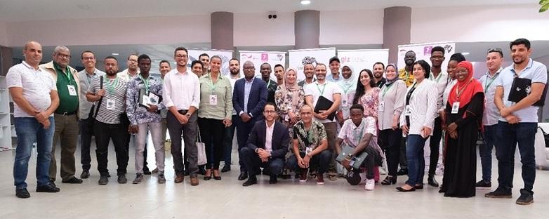 33 Workshopteilnehmer*innen verschiedener Diasporagruppen stehen für ein Gruppenfoto lächelnd nebeneinander.