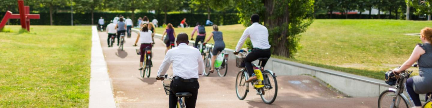 Zahlreiche Menschen in geschäftlicher Kleidung fahren mit Fahrrädern über einen hügeligen Weg.