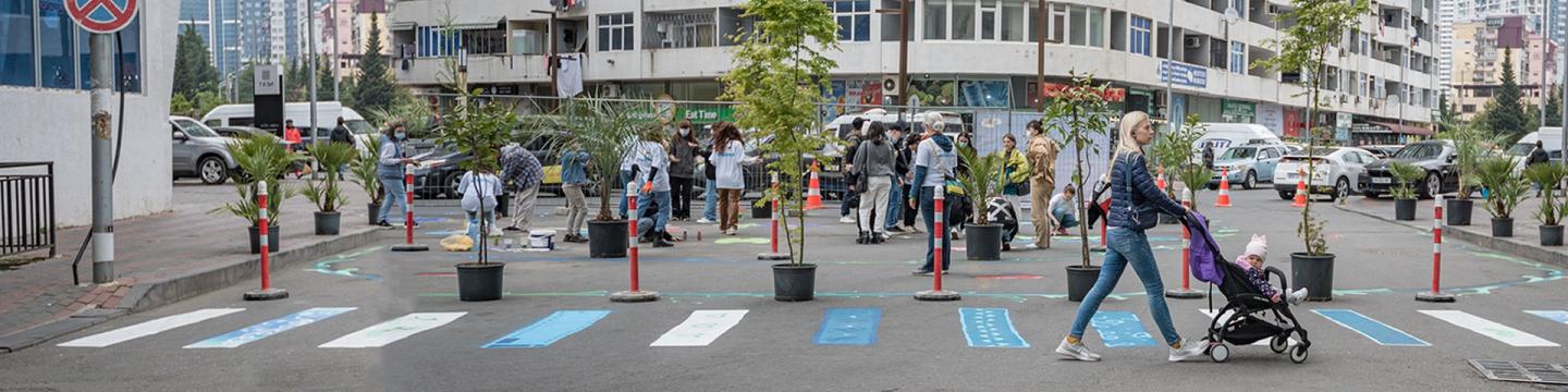 Menschen gestalten eine Straße in Tiflis, Georgien, zu einem fußgängerfreundlichen Bereich mit Topfpflanzen, bemalten Zebrastreifen und Gemeinschaftsaktivitäten um.