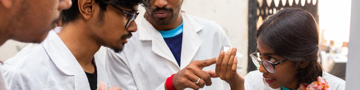 Mehrere Personen in Labor-Kitteln betrachten eine Probe in einer Schale.