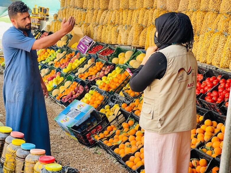 A member of staff from GOPA AFC talking to a trader at his fruit stand.