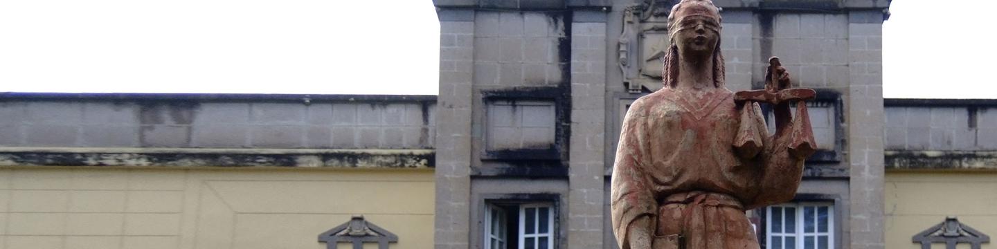 Eine Justitia-Statue steht vor einem Gebäude.