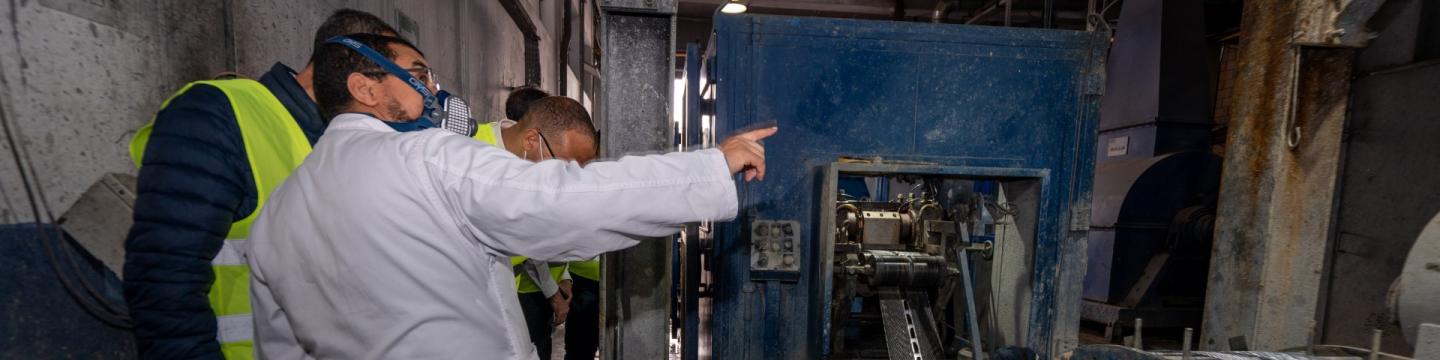 Eine Gruppe von Menschen steht in einer Fabrik neben einer Maschine.