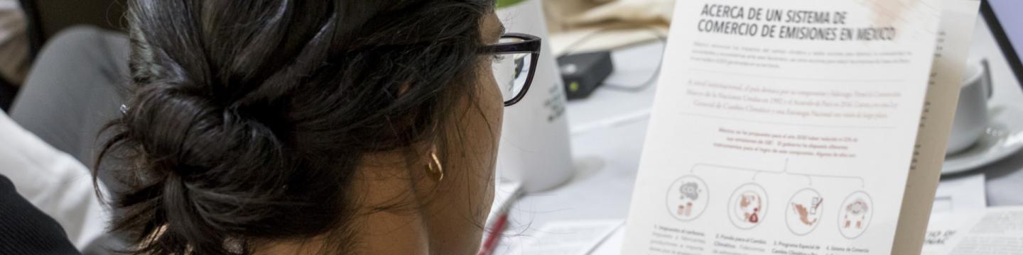 Una mujer lee un documento en español sobre el sistema de comercio de emisiones de México.