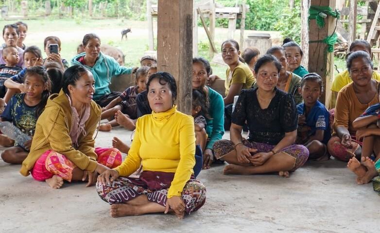 Women and children sitting in a rural community meeting, highlighting their reliance on forest resources for daily needs.