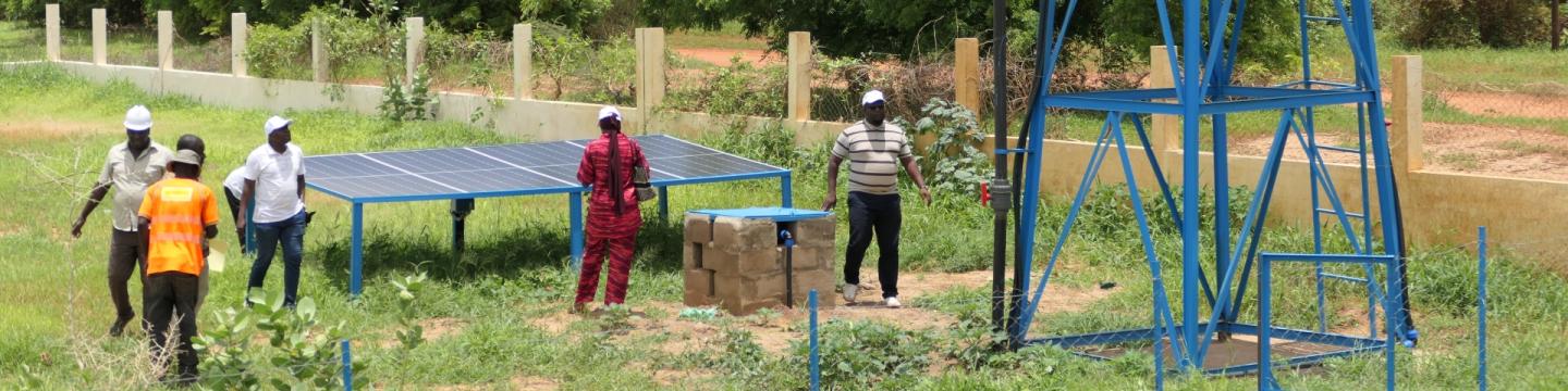 Menschen stehen auf einem Feld bei einem Wassertank, der mit einer Solaranlage betreiben wird.