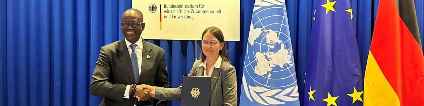 Lacina Koné, CEO von Smart Africa, und BMZ-Abteilungsleiterin Birgit Pickel geben sich vor den Flaggen der UN, der EU und Deutschland die Hand.