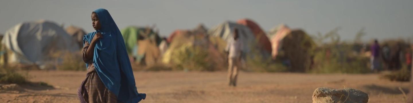 Eine Person mit einem blauen Schal geht in einem trockenen Gebiet in der Nähe von Zelten in einem Vertriebenenlager in Somalia.